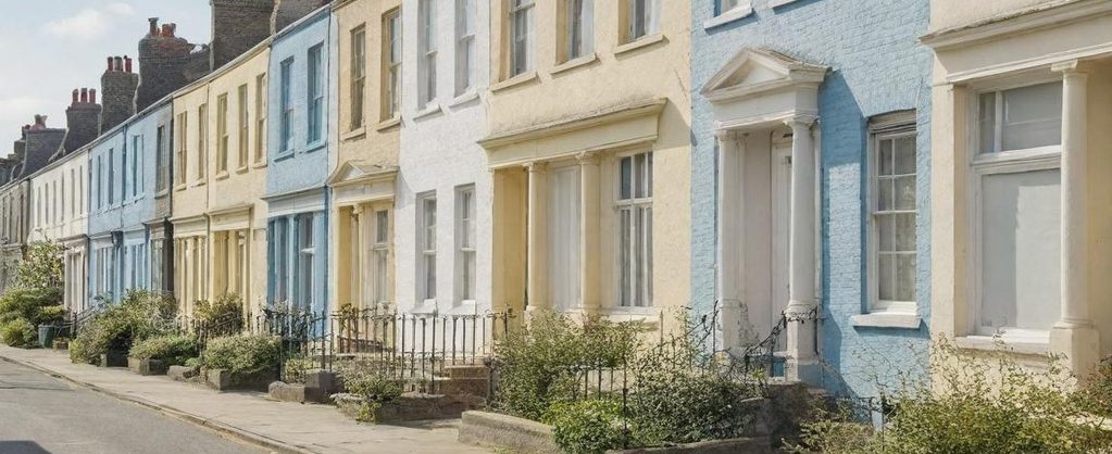 Row of terraced houses in pastel shades, lined with small front gardens.